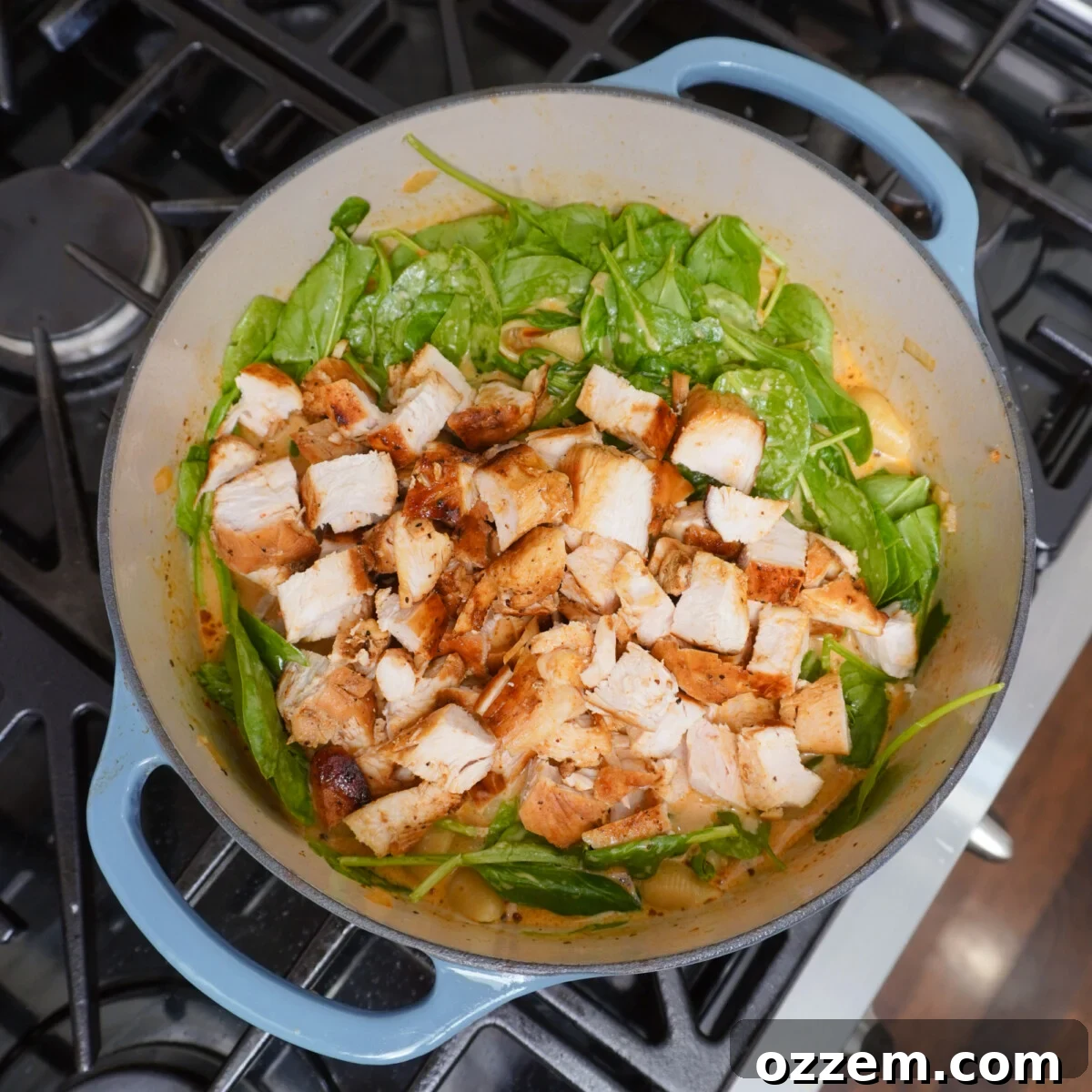 Chopped chicken and fresh spinach leaves being added to the simmering Marry Me Chicken Soup in a dutch oven.