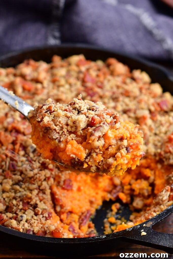 A spoonful of Smoked Sweet Potato Casserole with a crispy pecan crunch topping, showcasing its rich texture and tempting layers.
