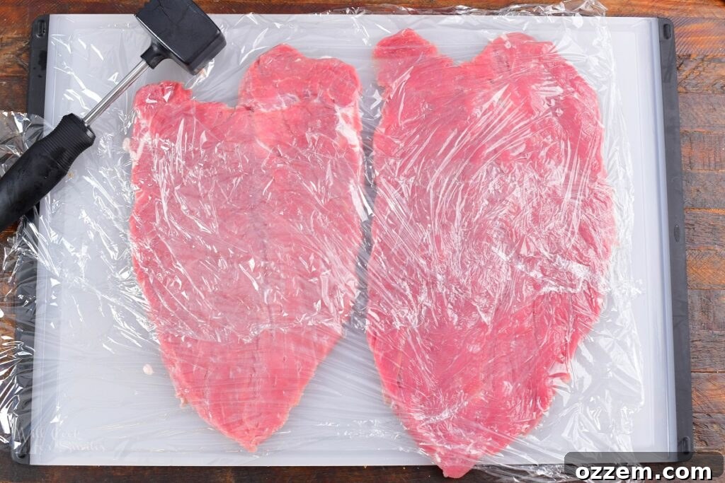 butterflied pork tenderloins covered in plastic wrap on cutting board