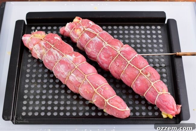 raw stuffed pork tenderloins wrapped in twine on metal grill basket