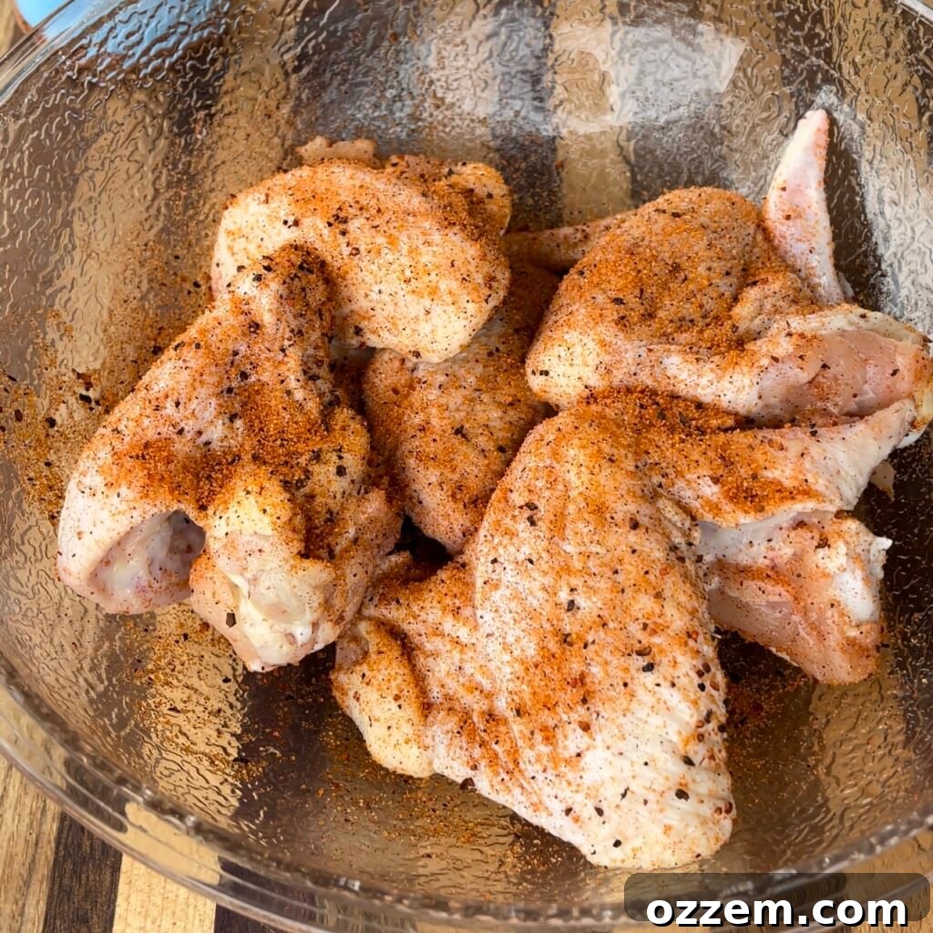 Chicken wings being tossed in olive oil and seasoned with BBQ rub in a bowl.