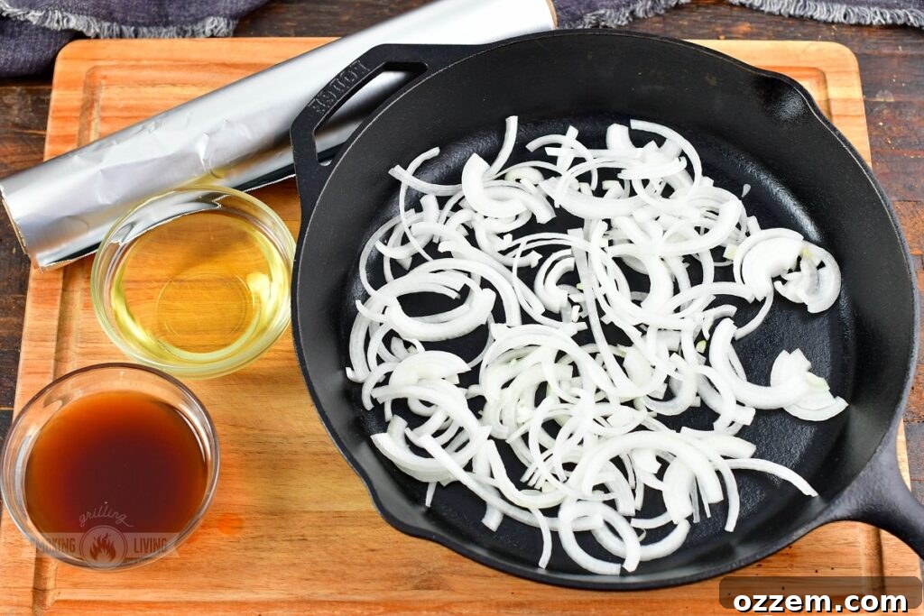 Sliced yellow onions, a bottle of apple juice, and a carton of beef stock arranged next to a skillet, ready for the smoking process