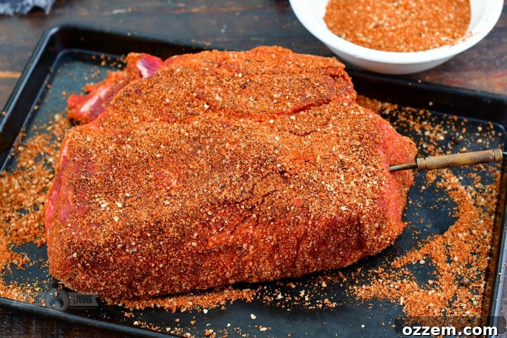 A beef chuck roast, generously seasoned and equipped with a leave-in thermometer probe, ready for the smoker