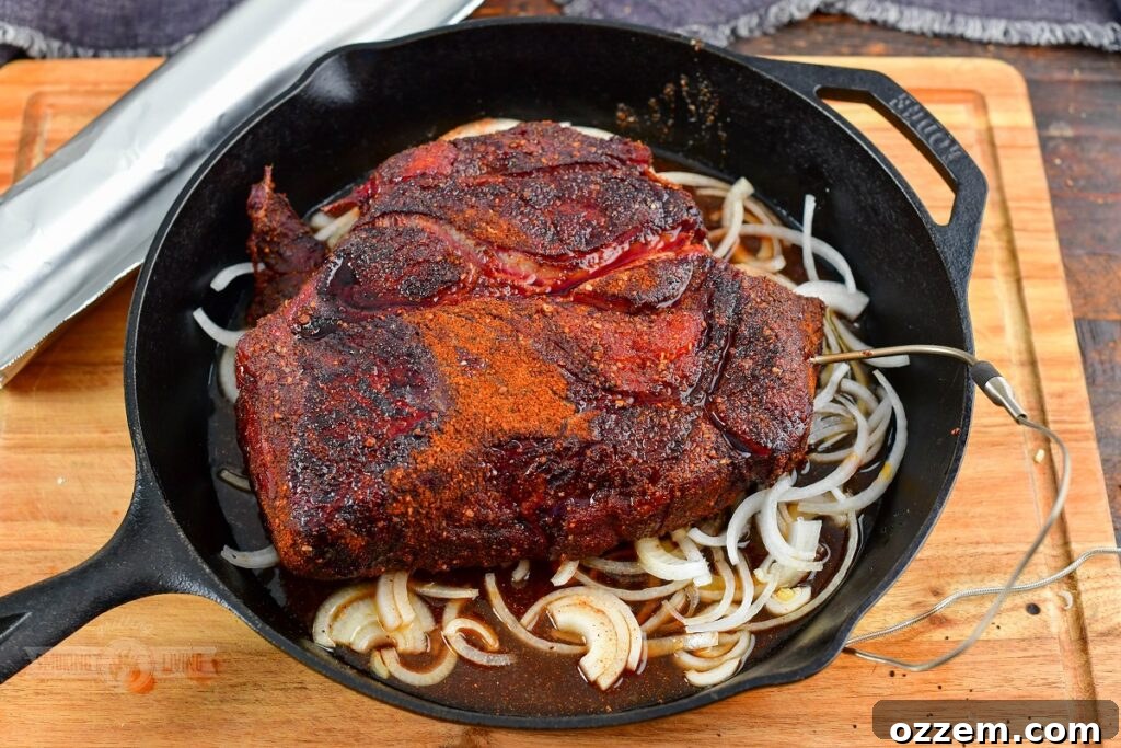 A seasoned beef chuck roast resting on a bed of sliced onions with cooking liquids in a skillet, preparing for the next phase of smoking