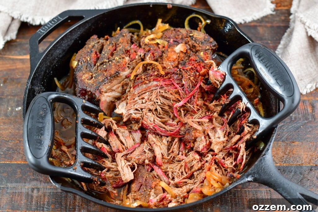 Meat claws actively shredding incredibly tender smoked beef chuck in a skillet, showcasing its perfect pull-apart texture