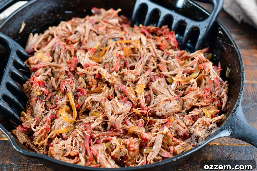 Close-up of perfectly pulled smoked beef chuck, shredded and glistening in its own juices within a cast iron skillet, with meat claws ready for serving