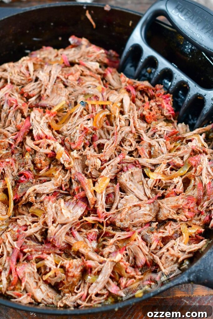 A large skillet brimming with shredded smoked pulled beef chuck, ready to be served, highlighting its rich color and tender texture