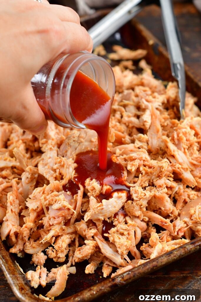 Smoked pulled chicken being sauced with BBQ sauce in a pan.
