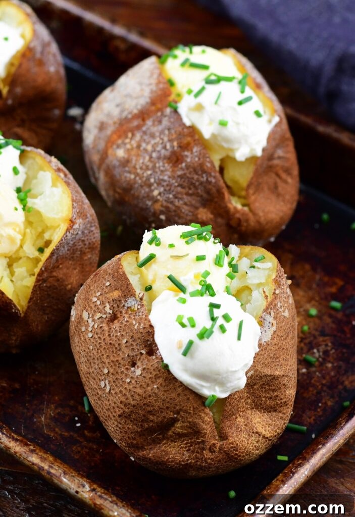 Smoked baked potatoes generously topped with melted butter and rich sour cream, showcasing their fluffy texture.