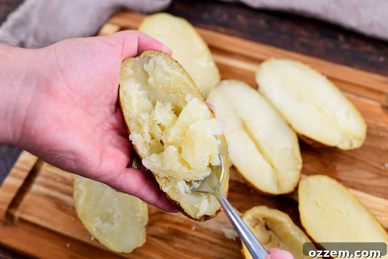 Smoky Creamy Twice Baked Potatoes 7 potato shells on a cutting board with a potato held while scooping meat out