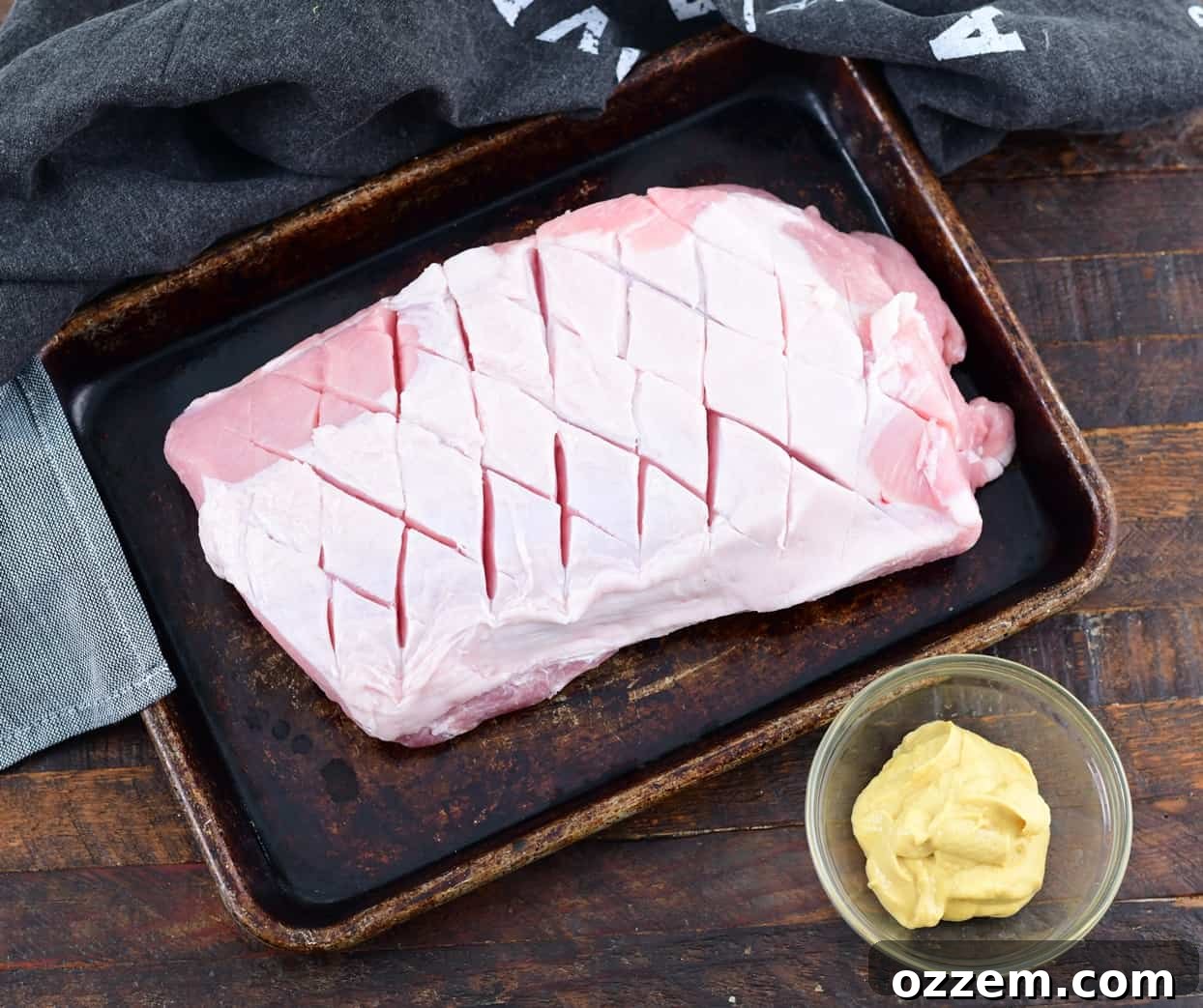 Wood-Fired Pork Loin Perfection 6 Applying Dijon mustard as a binder to the scored pork loin.