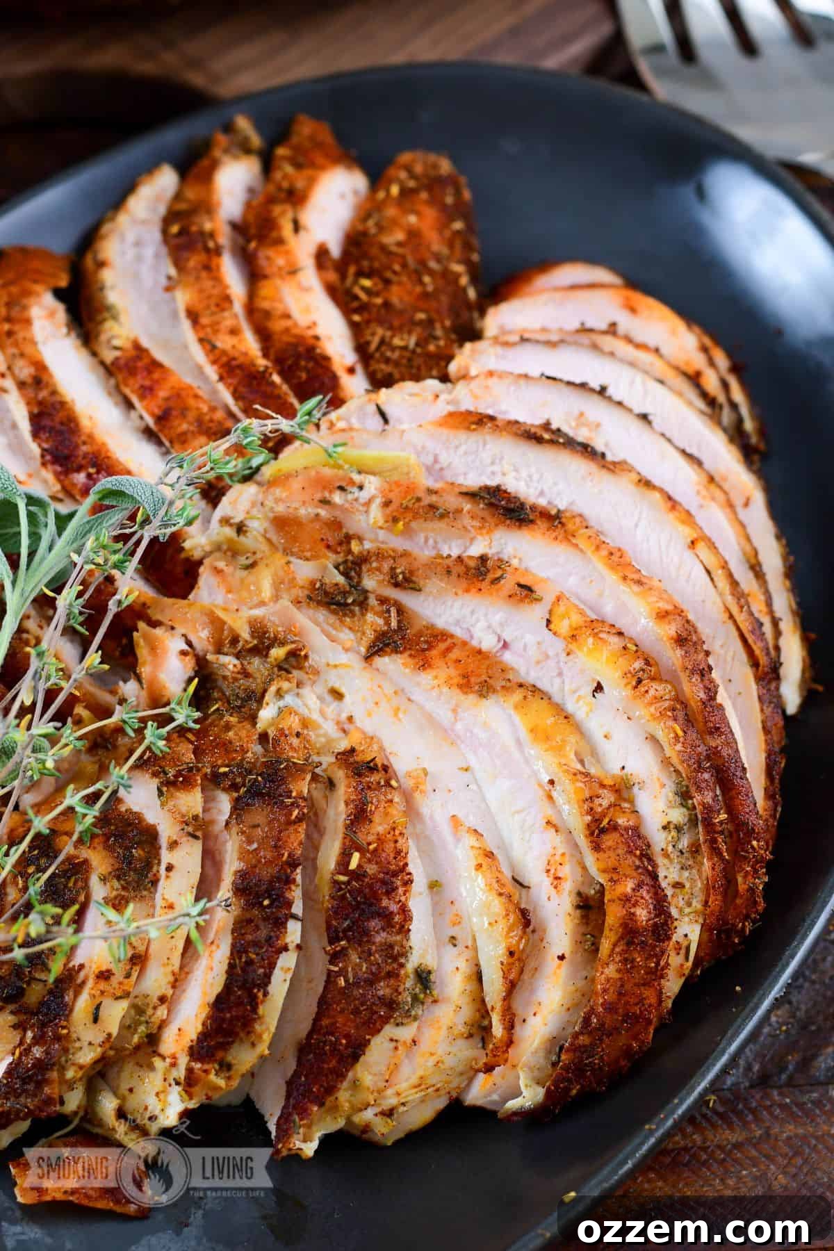 Thinly sliced smoked turkey breast, stacked artfully on a sleek black platter, garnished with fresh herbs, ready to be served.