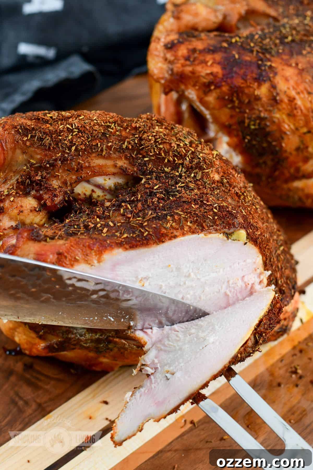A carving knife and two-pronged fork are used to thinly slice a perfectly cooked smoked turkey breast against the grain.