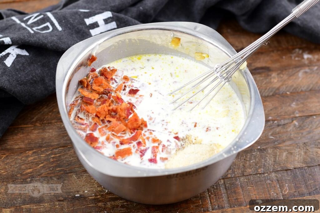 Decadent Smoked Scalloped Potatoes 5 A bowl of creamy, light orange sauce with visible flecks of bacon and onion, ready for scalloped potatoes
