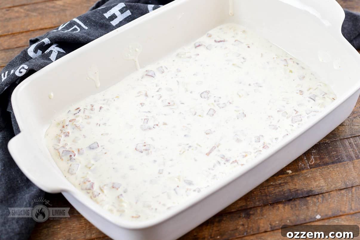 Decadent Smoked Scalloped Potatoes 7 A 9x13 ceramic baking dish with a thin layer of creamy sauce spread across the bottom