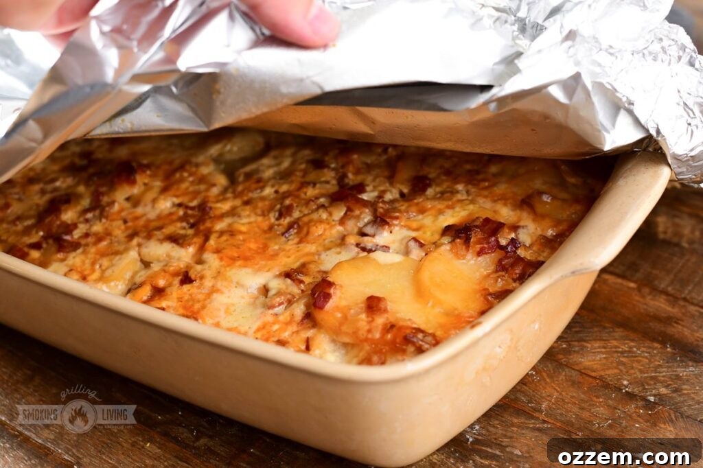 Decadent Smoked Scalloped Potatoes 10 Cooked Smoked Scalloped Potatoes in a white dish, with a corner of foil being gently pulled back to reveal the crispy, cheesy top