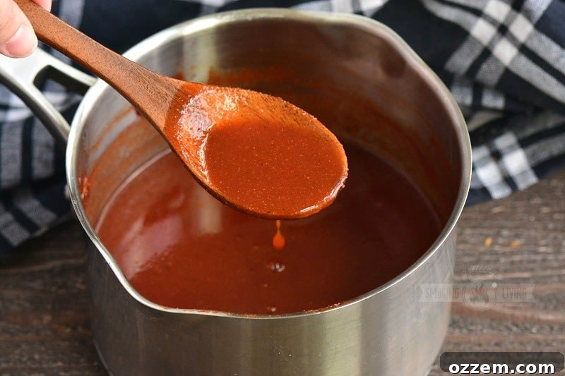 A spoon dipping into a pot of simmering homemade BBQ sauce, illustrating its rich texture and inviting aroma.