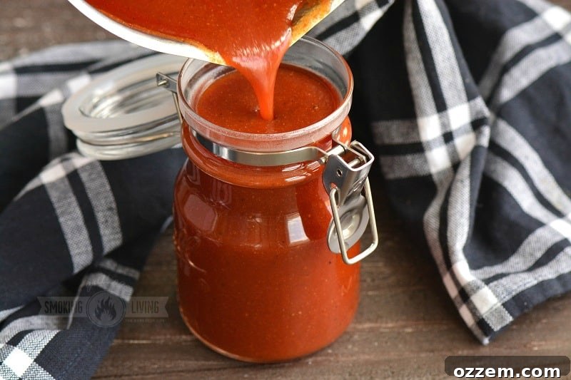 Cooked homemade BBQ sauce being poured from a pot into a glass jar, highlighting its luscious texture.