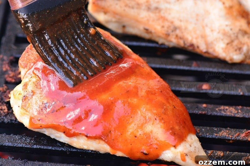 Grilled chicken being brushed with a thick layer of homemade BBQ sauce, showing its appetizing glaze.
