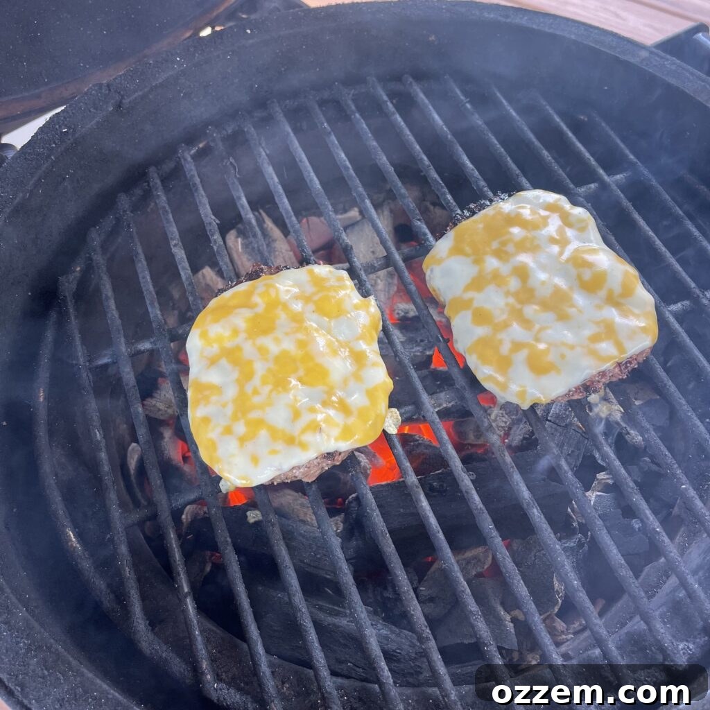 Two venison beef patties grilling on direct heat, topped with melted Colby Jack cheese, achieving a perfect golden-brown sear.