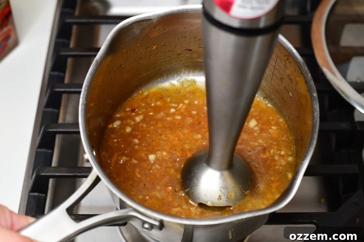 Sauce in a sauce pan being blended by a hand held blender.