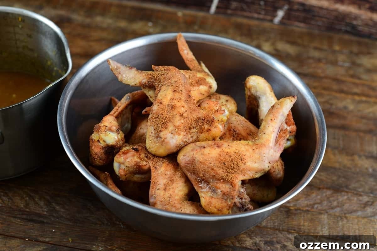 Smoked wings in a metal bowl with sauce to the left.