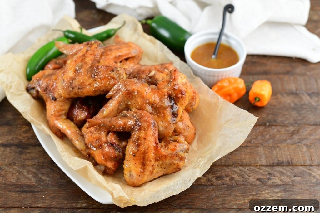 Sauced smoked bourbon peach wings on paper on a plates with additional sauce and pepper to the right.