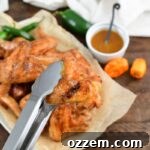 Tongs holding sauced smoked bourbon peach wings.