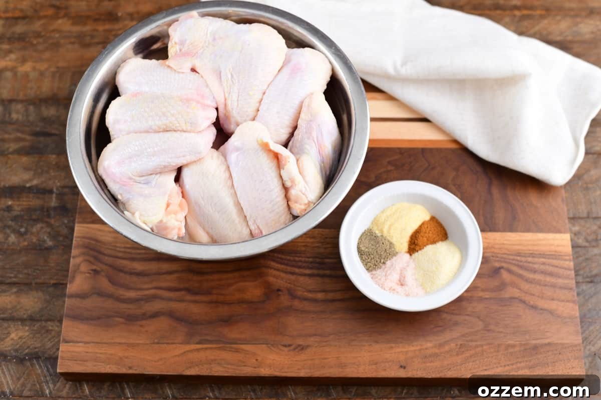 Raw wings in a metale bowl before being seasoned. Seasoning to the right in a small white cup.
