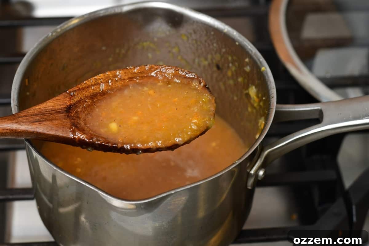 Spoon holding cooked sauce above a medium sauce pan.