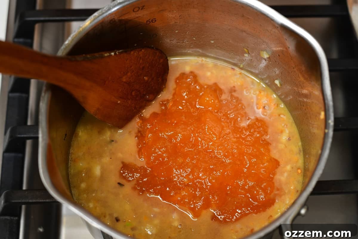 Peach preserves added to cooking sauce in a medium sauce pan.