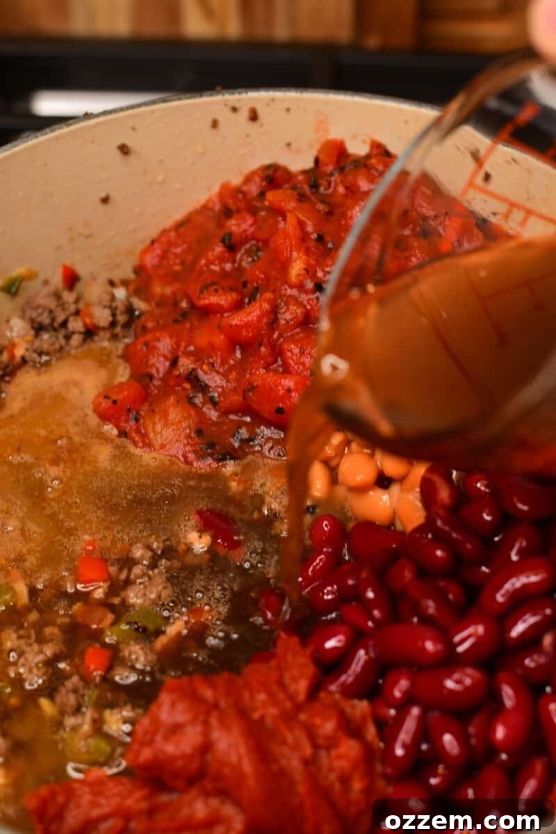 Beef stock being poured in the chili.