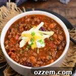 Smoked chili in a white bowl topped with sour cream and cheese