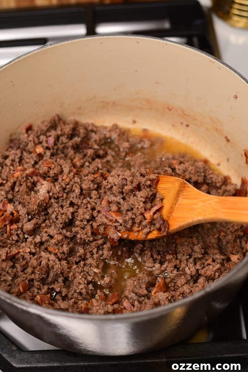 Spoon holding cooked ground beef and bacon in pot on stove