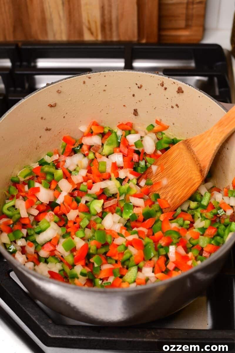 Raw peppers and onions in pot being cooked.