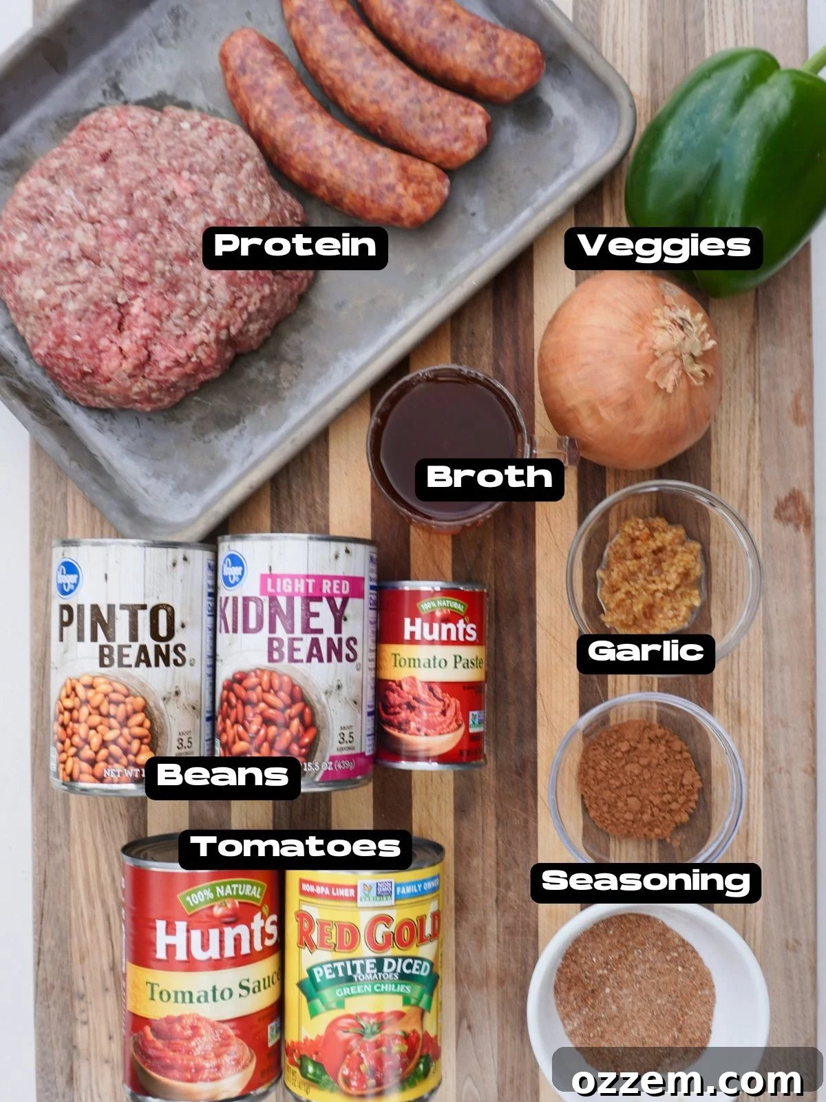 A vibrant selection of fresh ingredients laid out, including ground beef, Italian sausage links, various spices, diced vegetables, and canned goods for making a hearty chili.