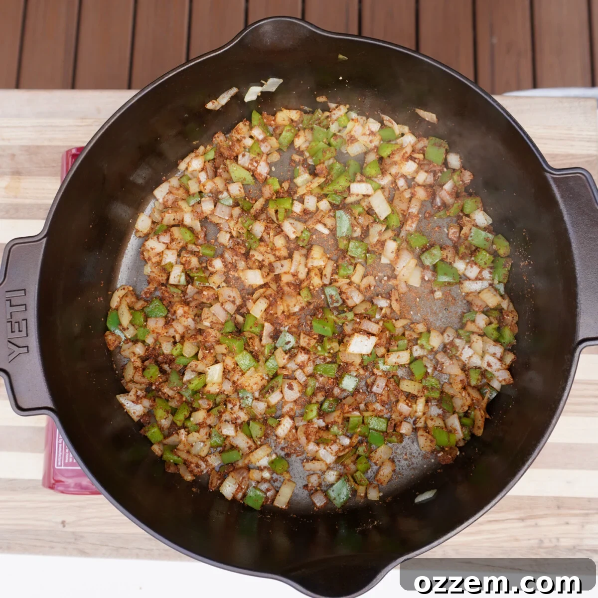 Diced onions and bell peppers being sautéed in a dutch oven with spices, forming the flavorful base of the chili.
