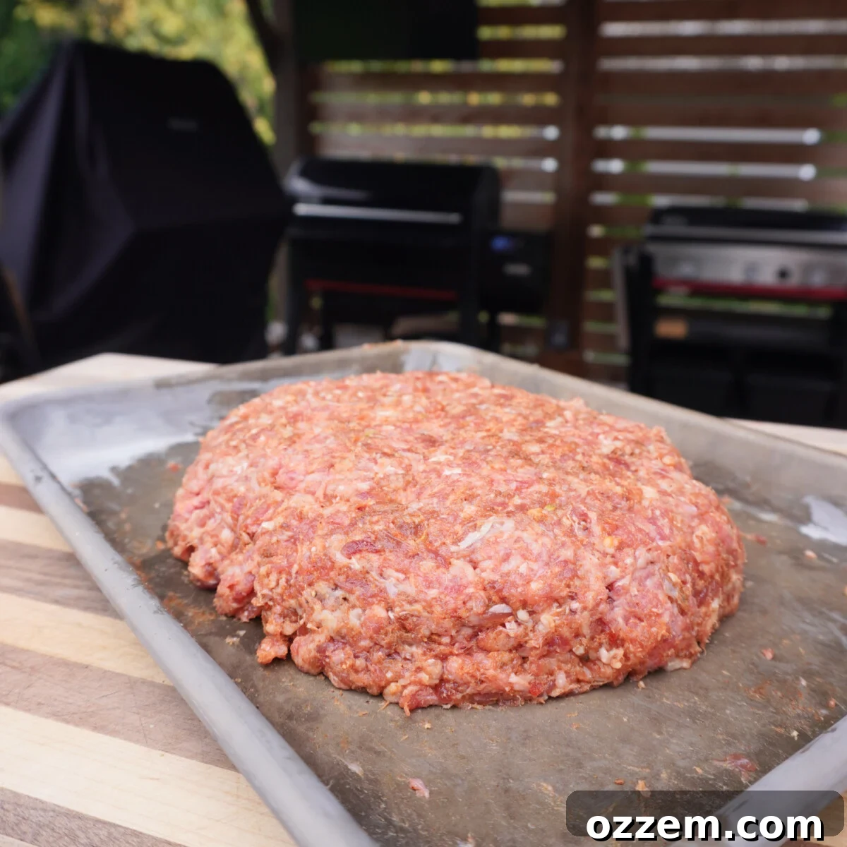 A large, flat beef patty seasoned and ready for smoking, placed on a cutting board.