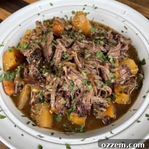 A close-up image of a rich and savory Pumpkin Beef Stew, garnished with fresh herbs, in a white bowl.