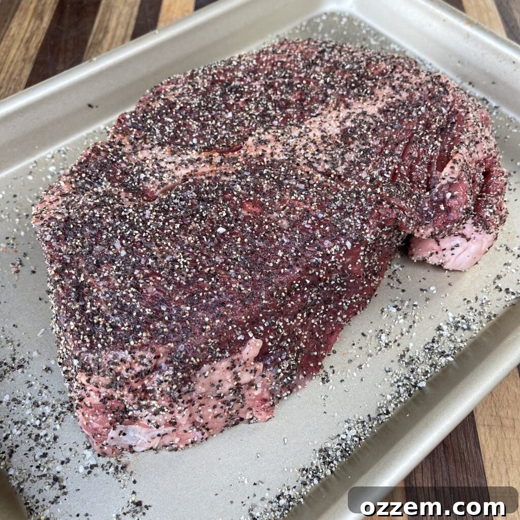 A generously seasoned chuck roast, glistening with a vibrant blend of spices, resting on a cutting board, ready for the smoker.