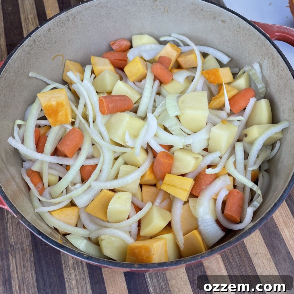 A Dutch oven filled with an assortment of neatly diced vegetables, including pumpkin, potatoes, carrots, and onions, ready for the next stage of cooking.