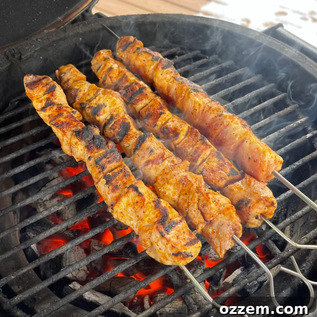 Bourbon chicken skewers sizzling on a hot grill, flames licking the edges, with a brush ready to apply glaze.