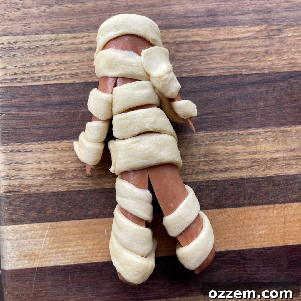 Monster Mummy Bites 4 Hot dogs wrapped in crescent roll strips, resembling mummies, before cooking