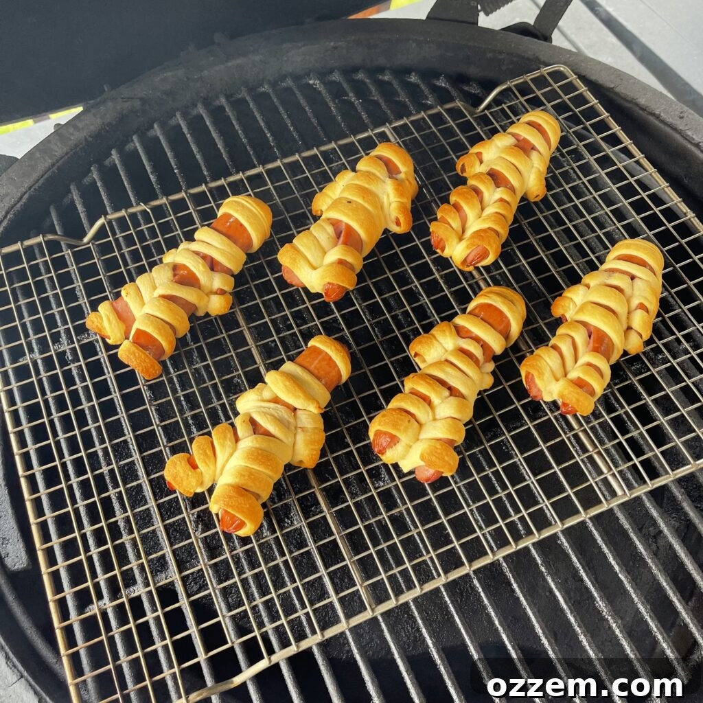 Monster Mummy Bites 5 Mummy dogs cooking on a wire rack on a grill with indirect heat