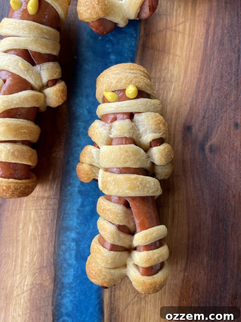 Monster Mummy Bites 6 Finished mummy dogs with yellow mustard eyes served with a side of black raspberry dipping sauce