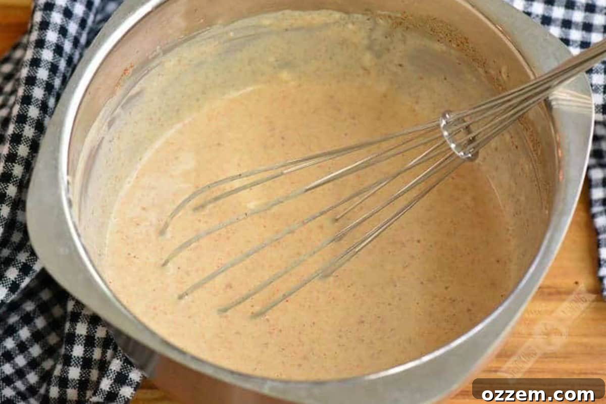 Southern Creamy White BBQ 4 White BBQ sauce in a metal bowl with a metal whisk on a wood surface.
