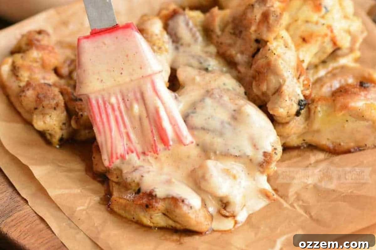 Southern Creamy White BBQ 6 Brushing white BBQ sauce onto grilled chicken that is on wax paper.