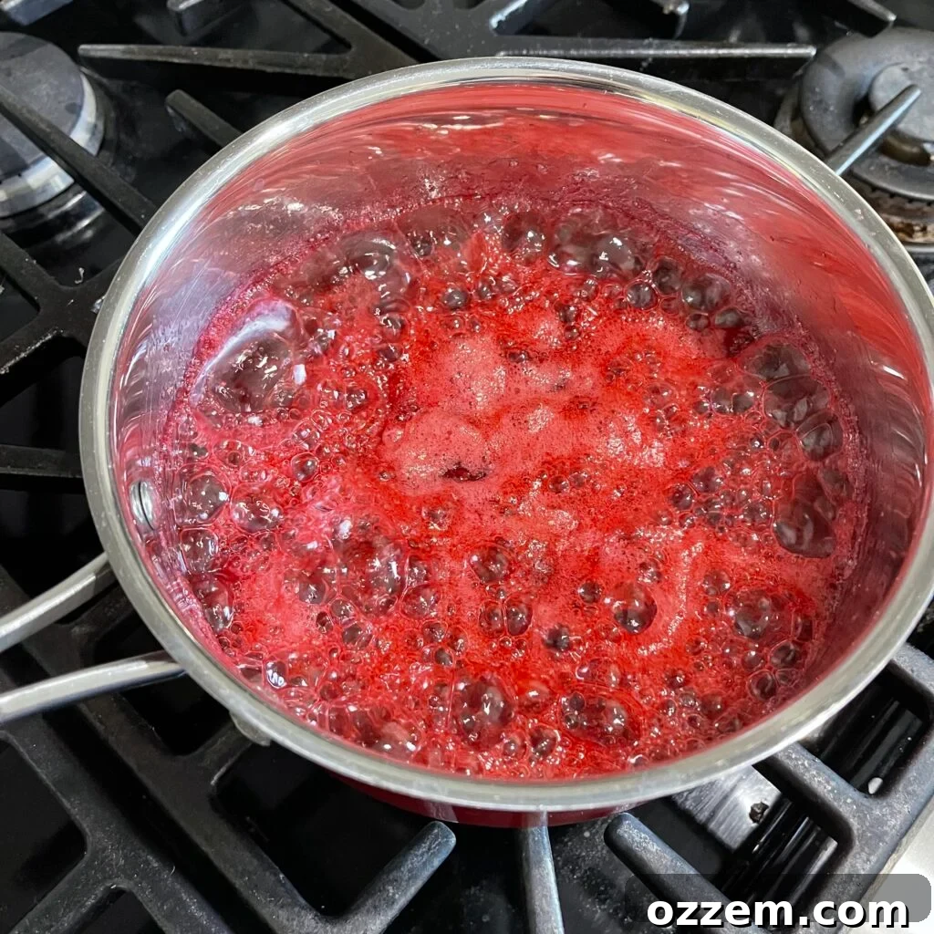Cranberry sauce simmering gently on the stove with orange zest and cinnamon stick visible.