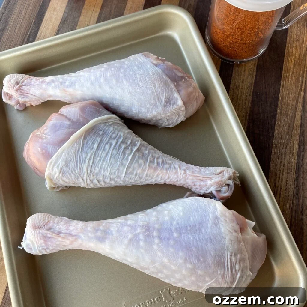 Raw turkey legs being seasoned generously with a dry rub and olive oil binder.