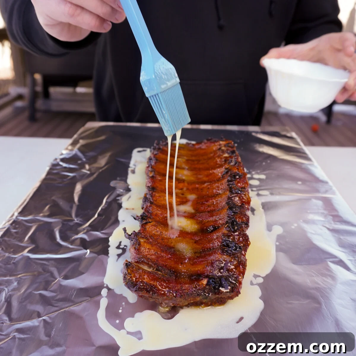 Succulent Slow-Smoked Baby Back Ribs 9 Melted butter being drizzled over smoked ribs on aluminum foil.